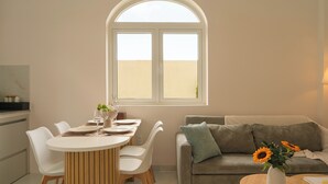 Uma área de refeições com uma mesa redonda, cadeiras brancas e uma janela acima.