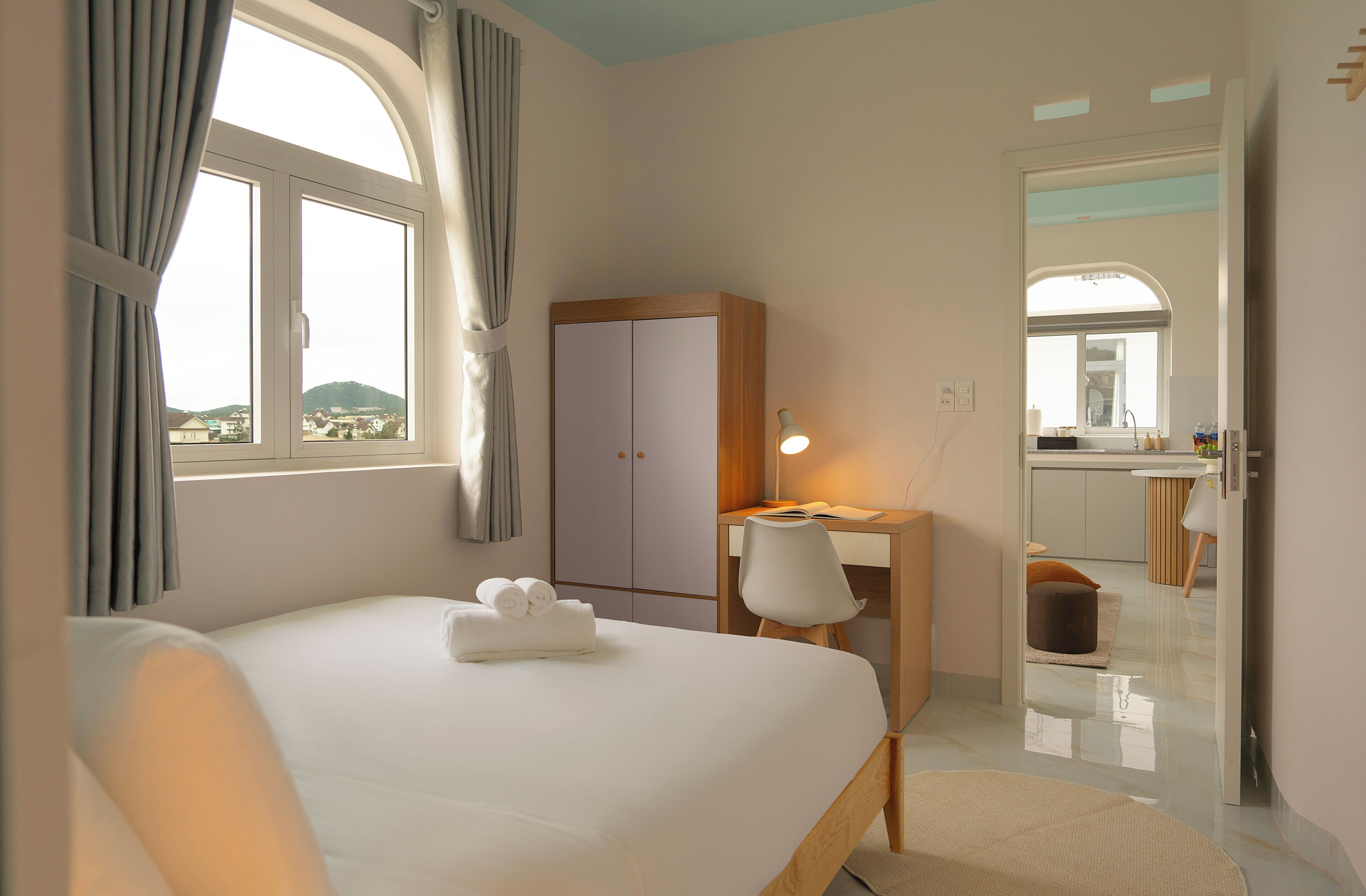 A hotel room with a bed, a desk, a wardrobe, and a bathroom visible through an open door.