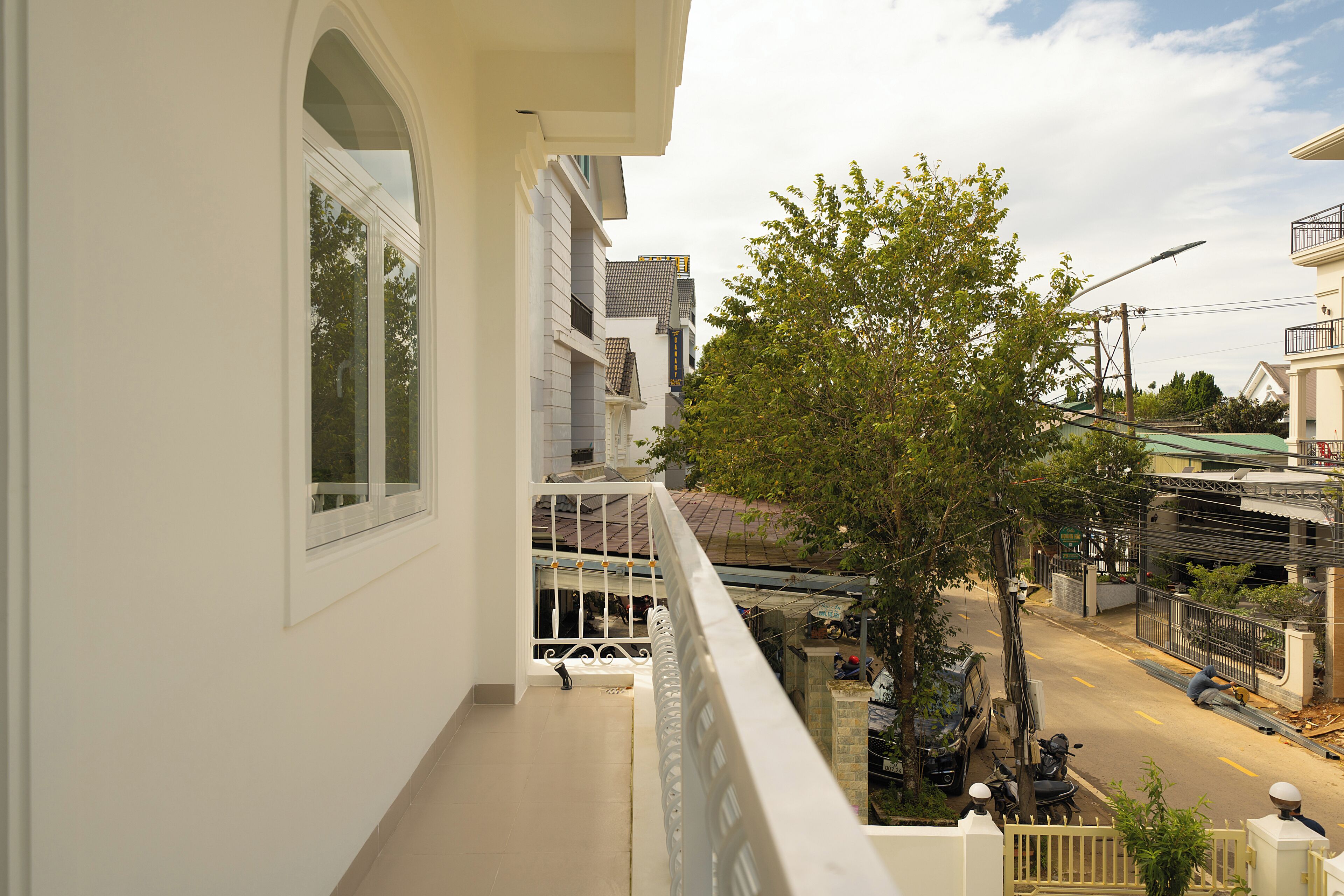 A residential balcony with a view of the street below, a tree, and a parked motorcycle.