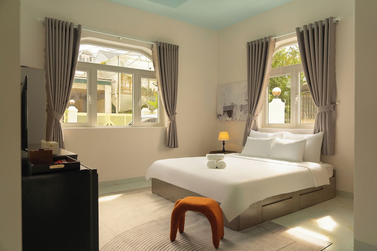 Een hotelkamer met een bed, een bureau, een lamp en een raam met gordijnen.