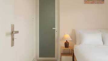 Une chambre à coucher avec un lit, une table de chevet avec une lampe, une porte et un tableau au mur.