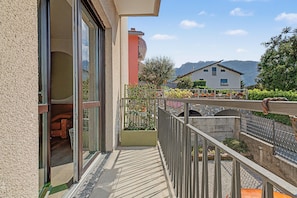 A balcony with a view of a mountain, a house in the background, and a clear sky.