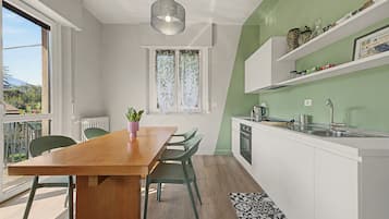 Eine moderne Küche mit einem Holztisch, grünen Stühlen und einem Fenster mit Blick ins Freie.