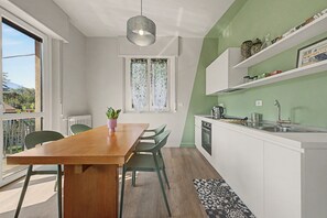 A modern kitchen with a wooden dining table, green chairs, and a window with a view of the outdoors.