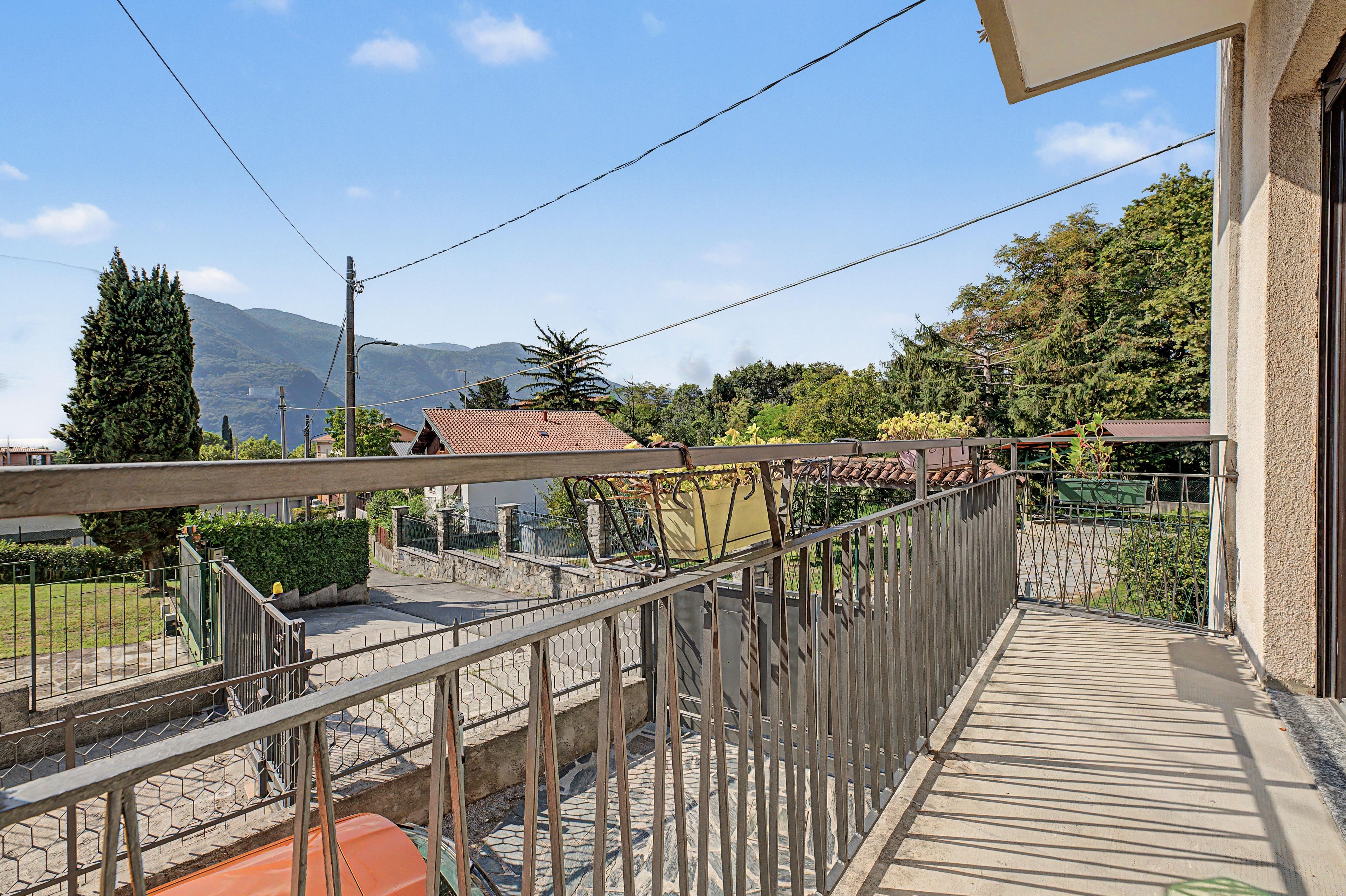 Un balcon donnant sur une montagne, un jardin et un bâtiment avec un toit en tuiles.