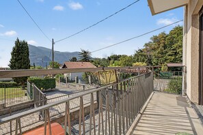 Un balcon donnant sur une montagne, un jardin et un bâtiment avec un toit en tuiles.