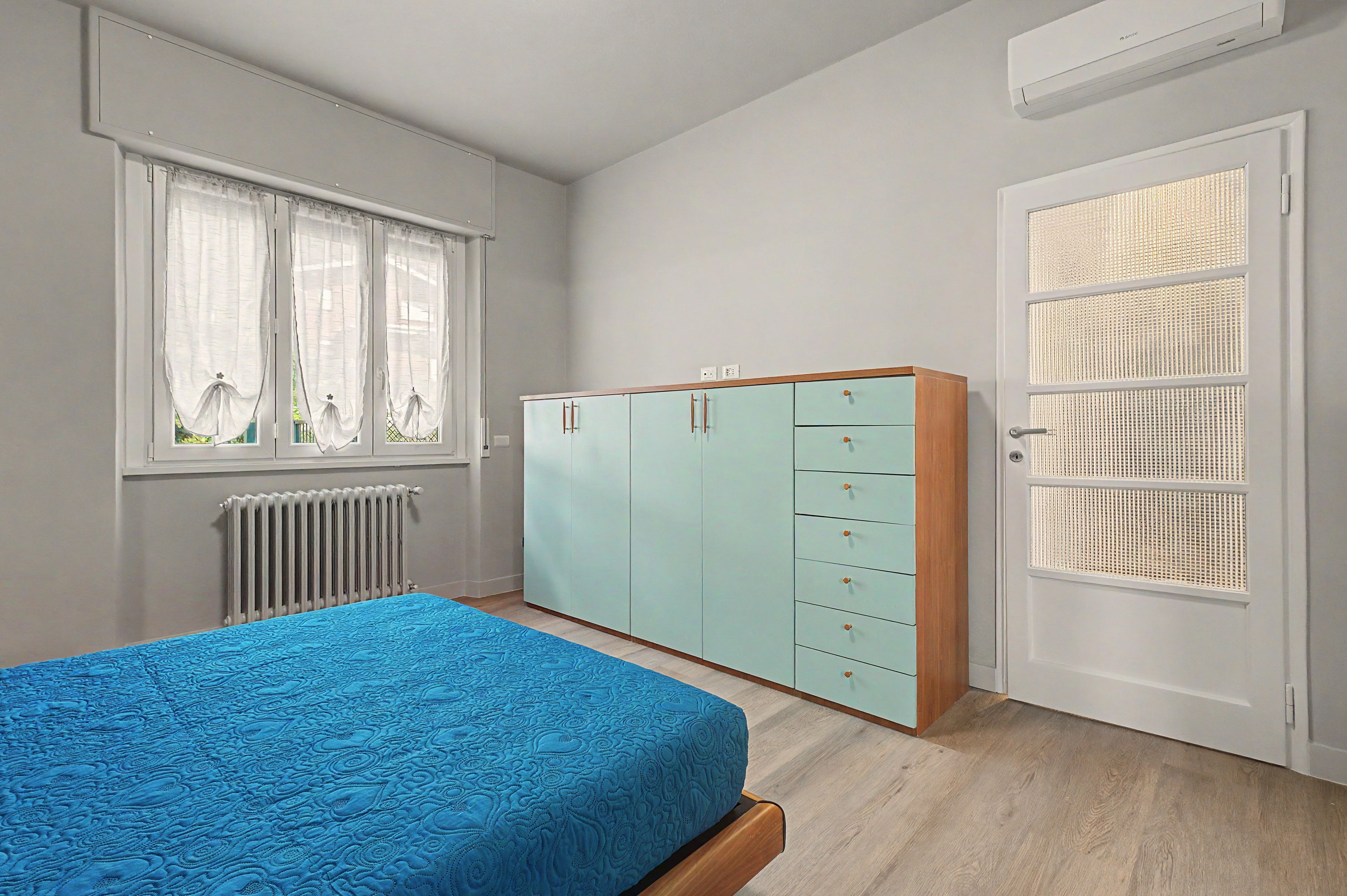 A bedroom with a bed, a wardrobe, a radiator, and a window with curtains.