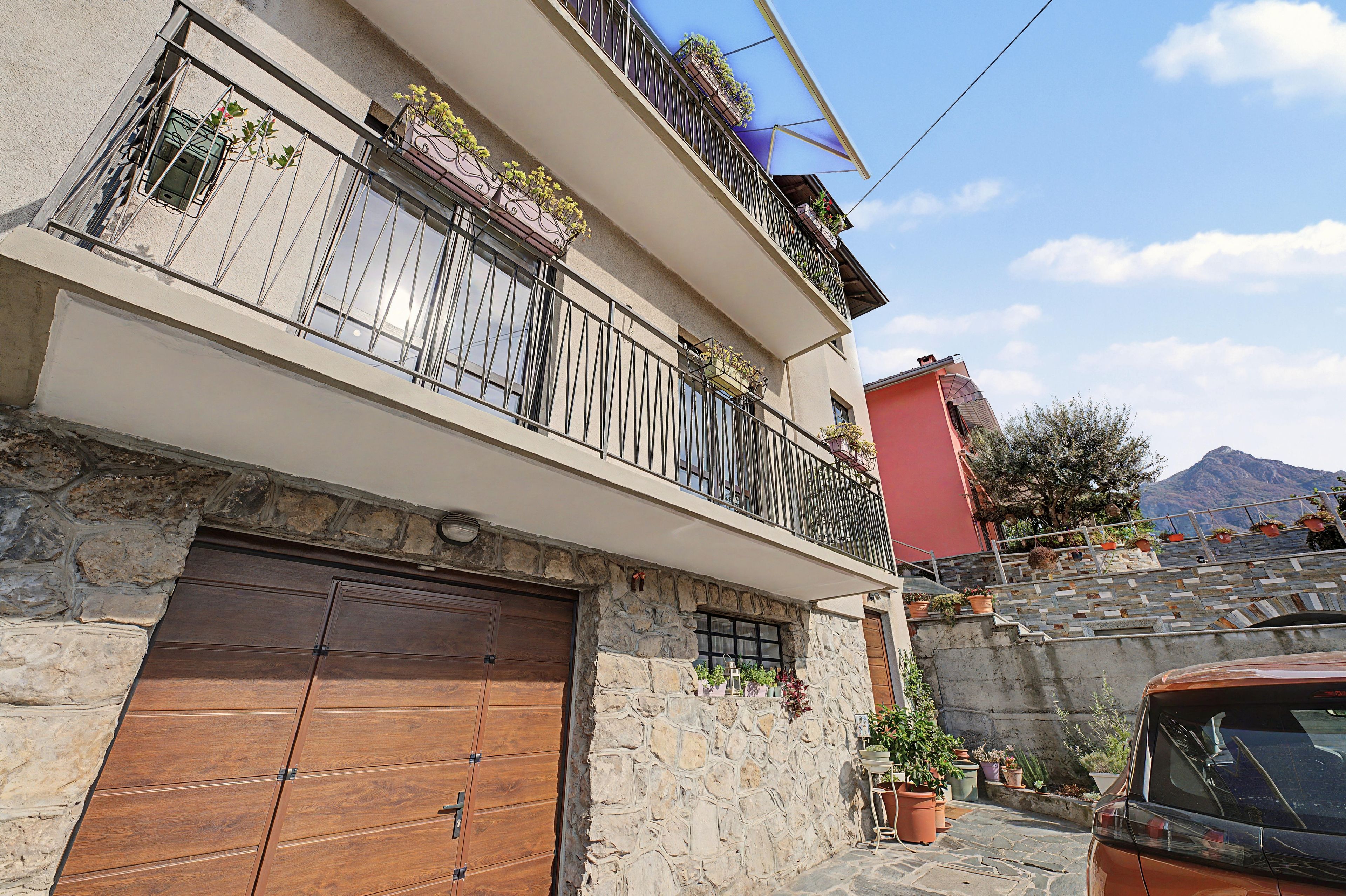 Un edificio a due piani con facciata in pietra, un portone in legno e un balcone con piante in vaso.