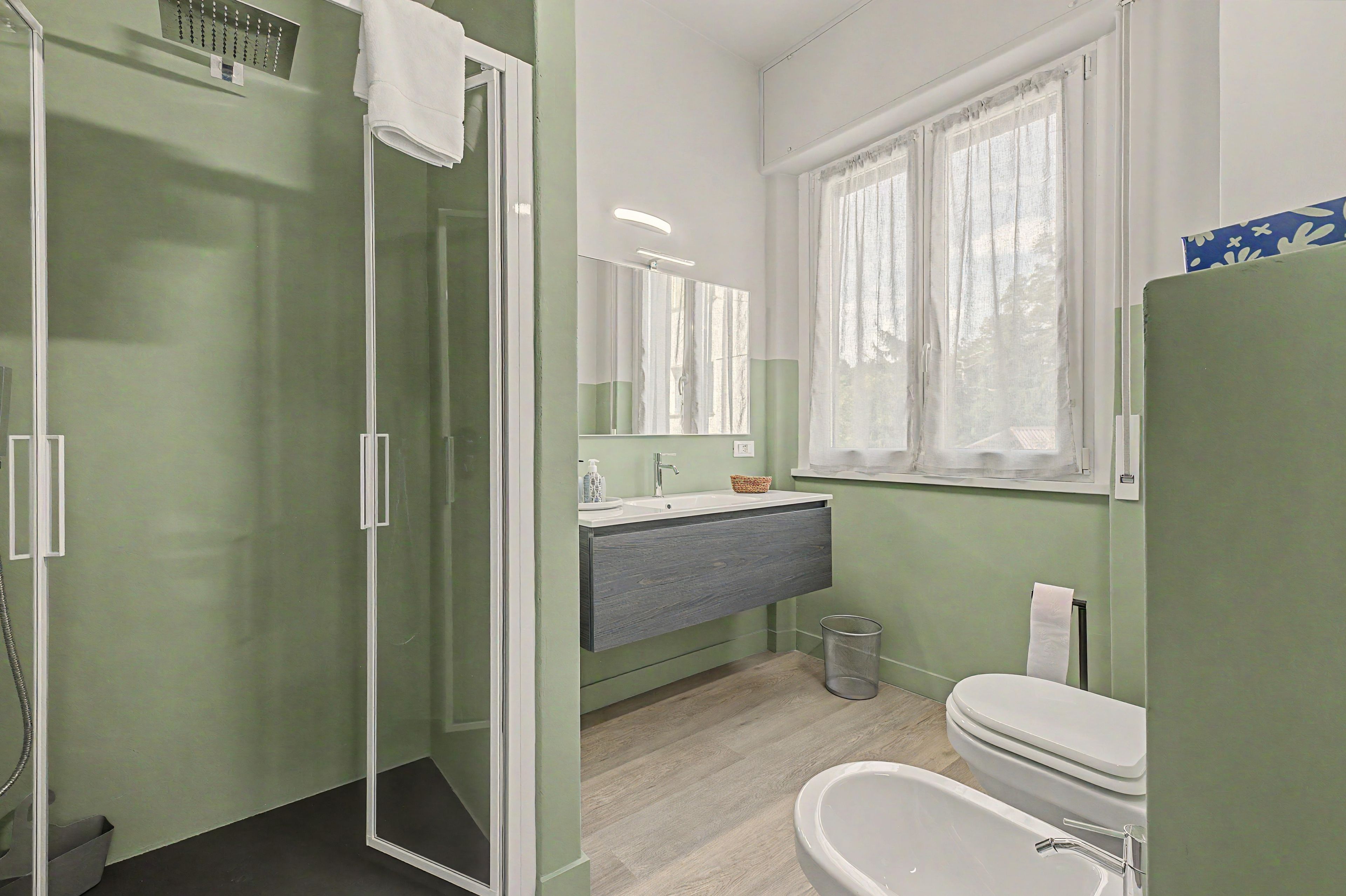 A bathroom with a shower, toilet, sink, and a window with curtains.
