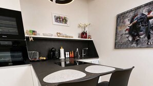 A modern kitchen with a black countertop, two black chairs, a white island, and a hanging light fixture.