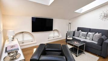Een moderne woonkamer met dakraam, een zithoek, een salontafel en een flatscreen televisie.