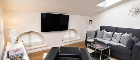 A modern living room with a skylight, a sofa set, a coffee table, and a flat-screen TV.