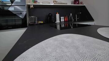 A modern kitchen with a black countertop, a white textured rug, and a wooden ceiling.