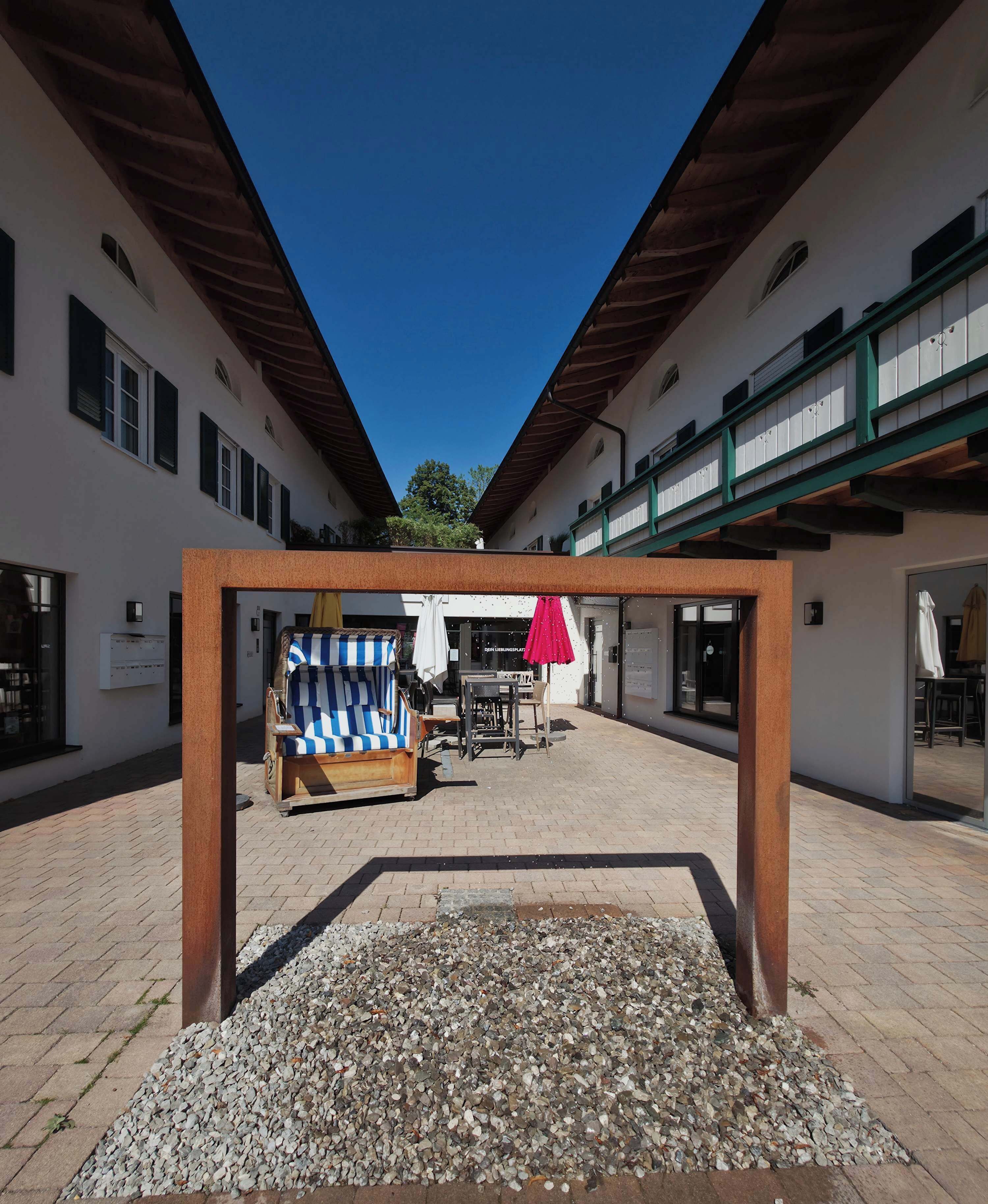 Een binnentuin met een houten pergola, een zithoek en een grindpad.