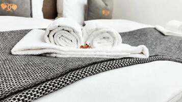 Een keurig opgemaakt bed met opgerolde witte handdoeken, een grijs beddegoed met patroon en passende kussens.