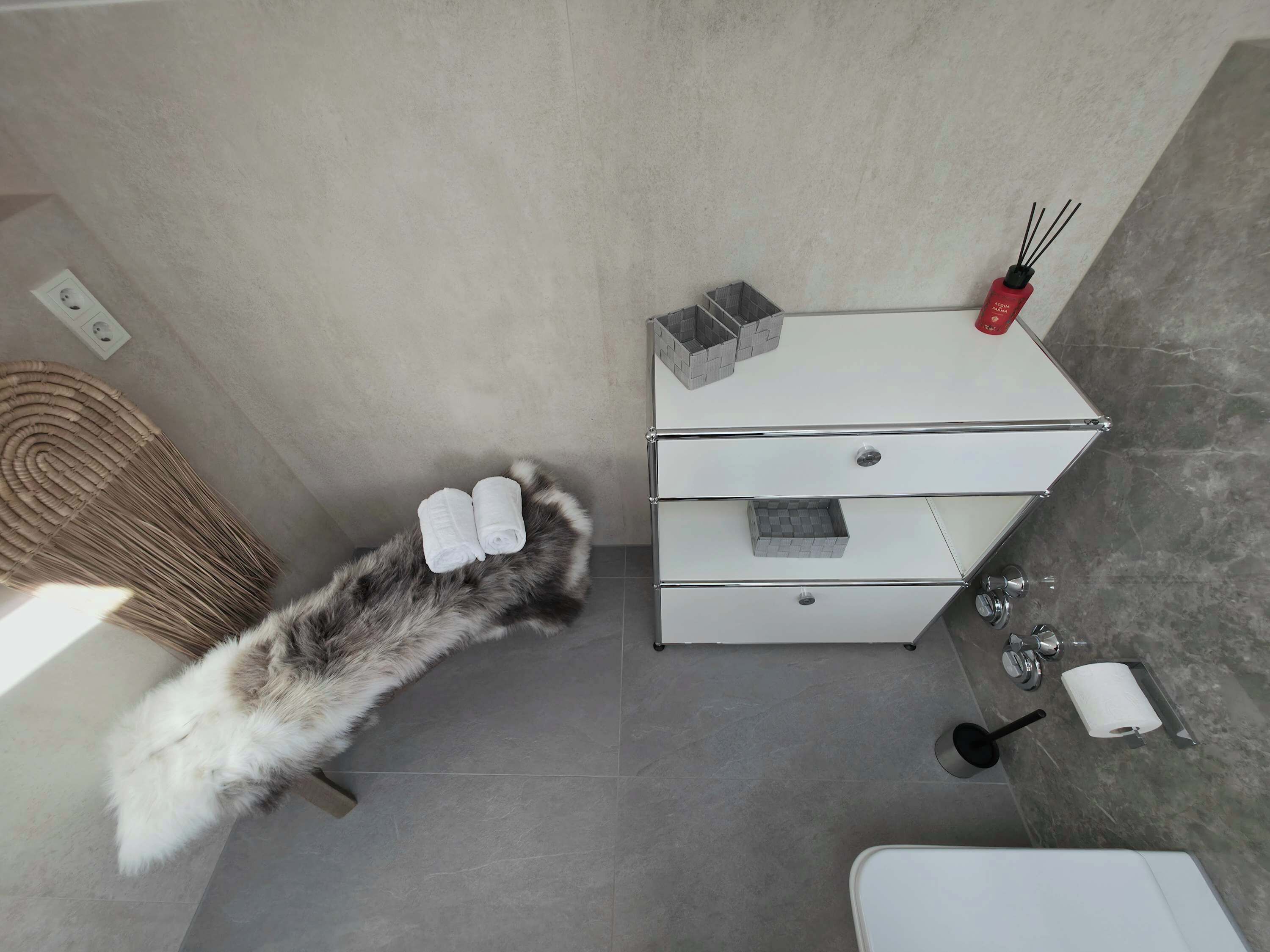 A bathroom with a white cabinet, a towel rack, a bottle of hand soap, and a toilet paper roll.