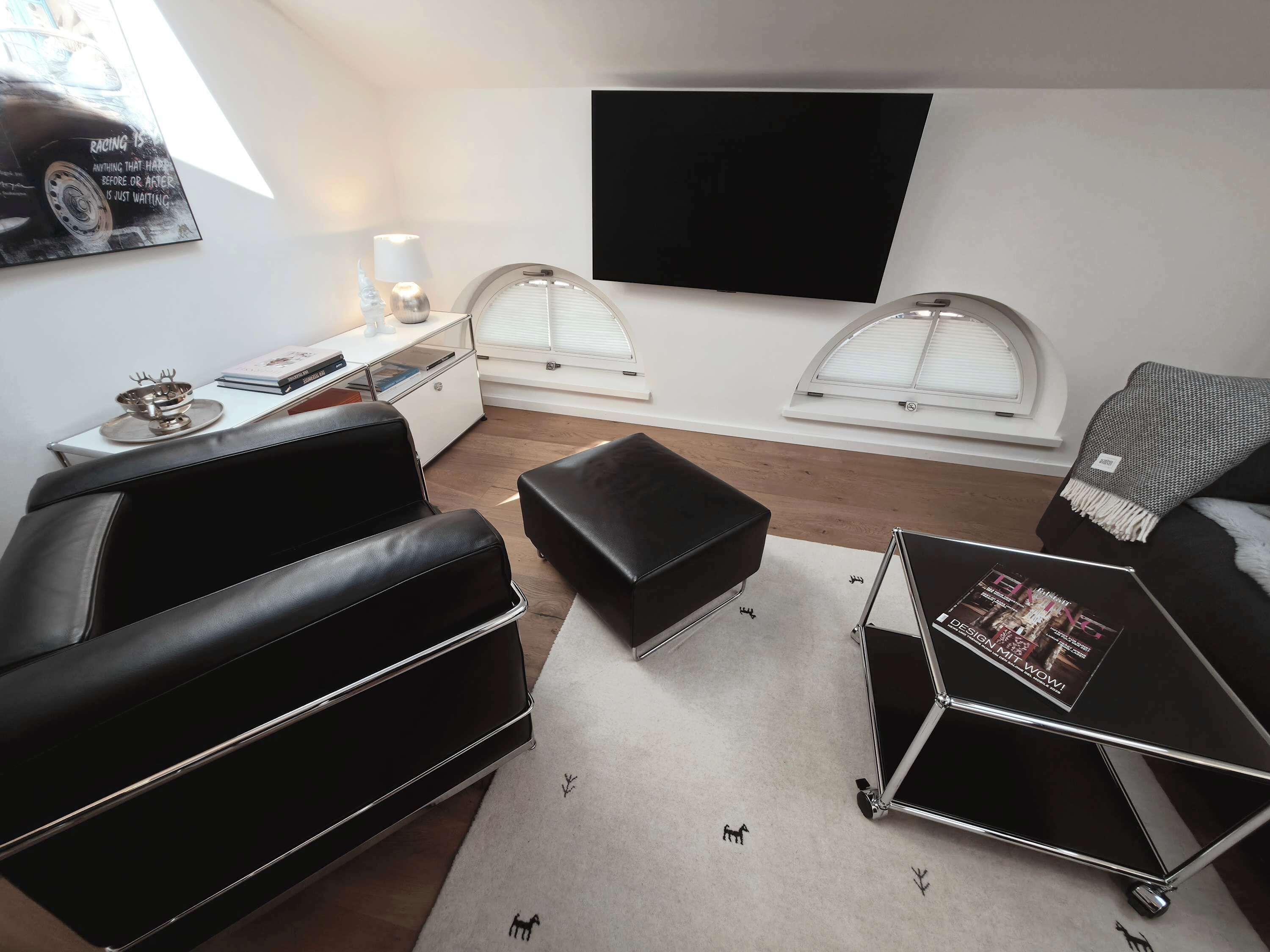 Ein modernes Wohnzimmer mit einer schwarzen Ledersofa, einem Couchtisch, einem flachbildschirmfernseher an der Wand und einem Fenster mit weißem Rollo.