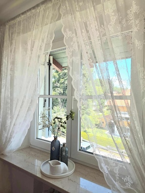 A window with lace curtains, a vase with flowers, and a marble ledge. - 2 min to Tegernsee, Balcony, Sauna, Modern Kitchen (Bad Wiessee)