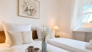 A hotel room with a large bed, a bedside table with a lamp, a framed picture on the wall, and a window with curtains. - 2 min to Tegernsee, Balcony, Sauna, Modern Kitchen (Bad Wiessee)