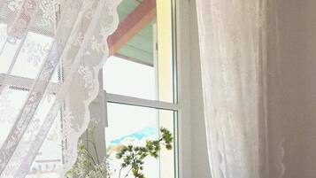 A window with lace curtains, two vases with flowers, and a small white dish on a marble ledge.