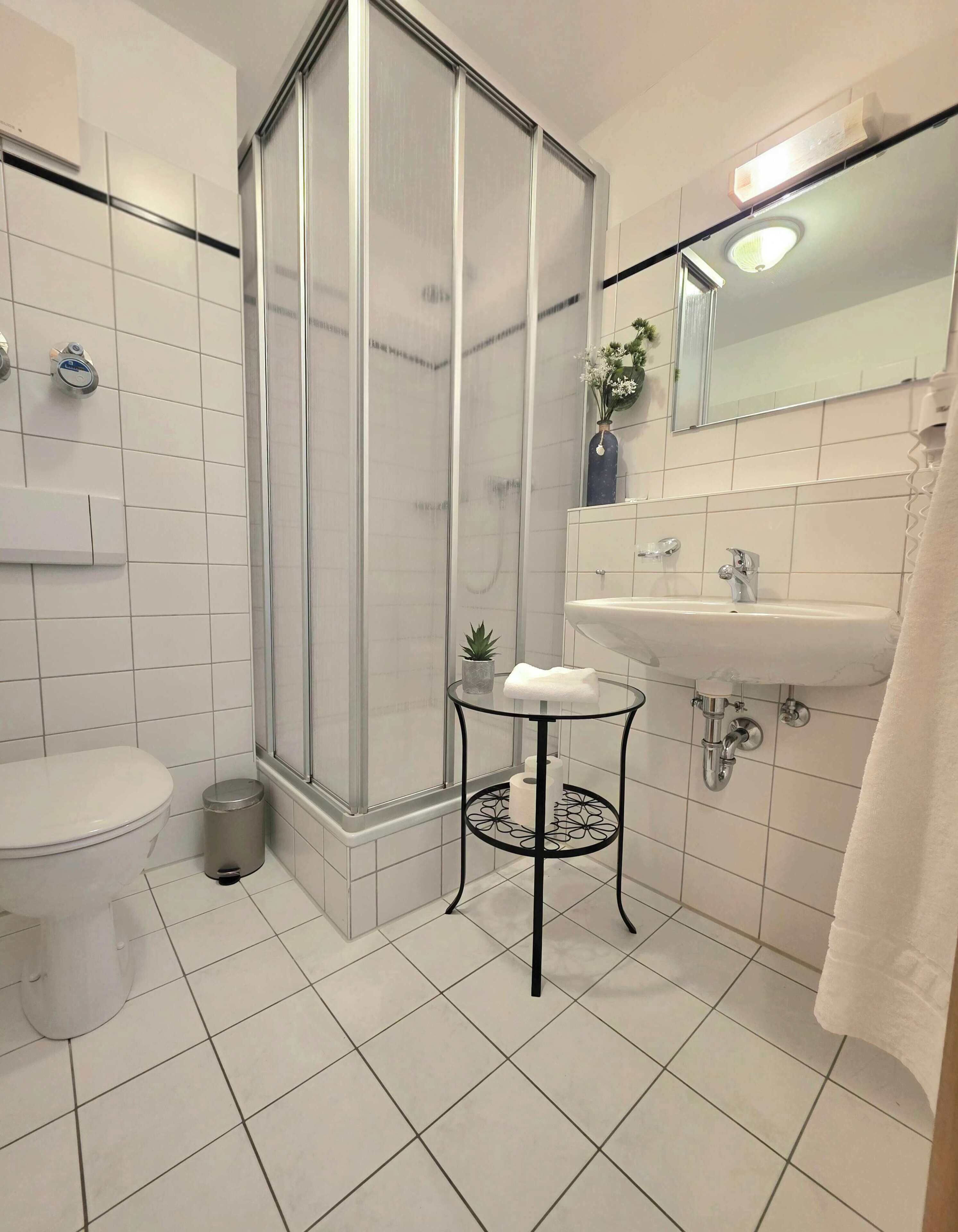 Een moderne badkamer met toilet, een douchecabine, een wastafel en een klein tafeltje met een handdoek.