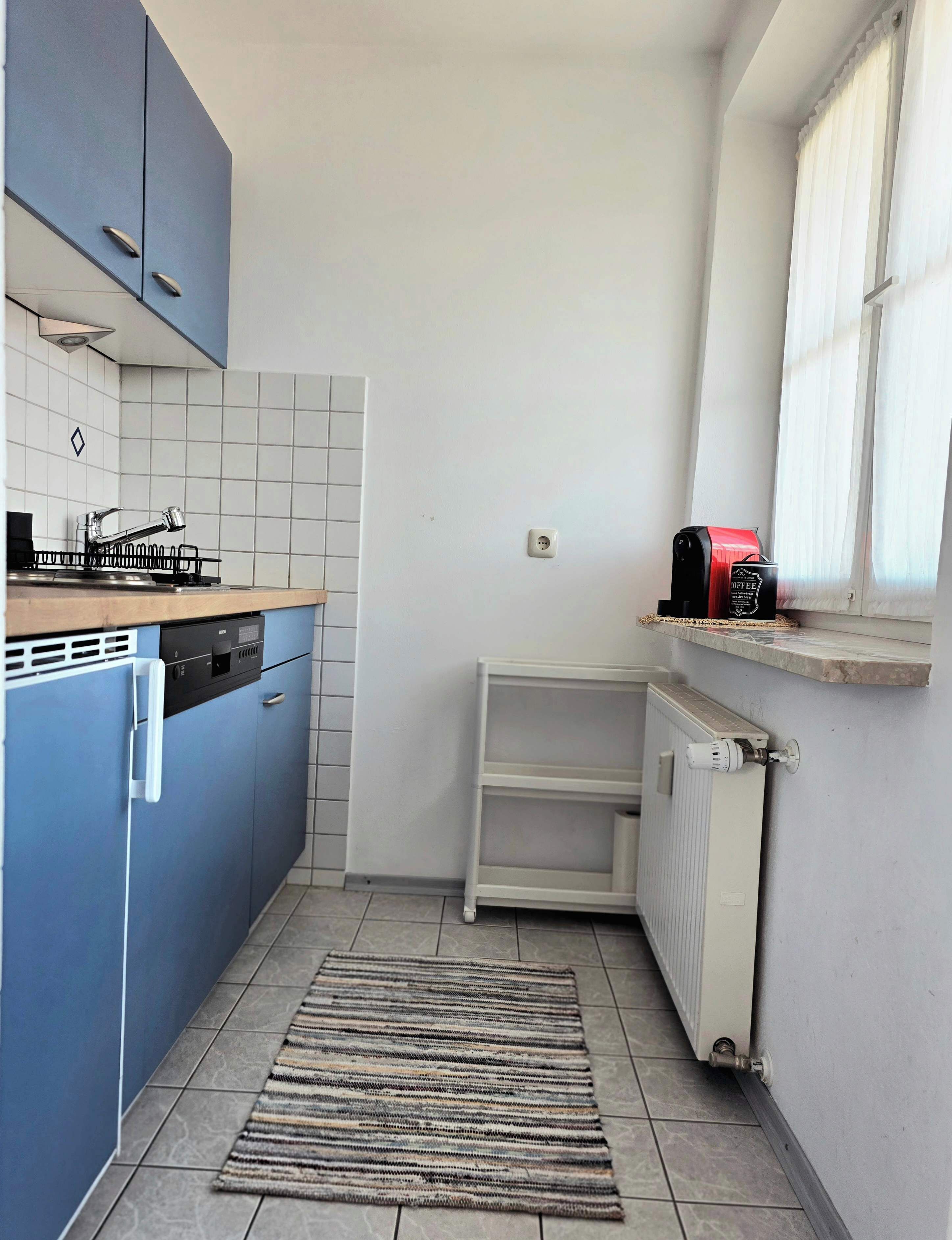 Cozinha compacta com armários azuis, cafeteira e radiador.