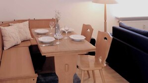 A dining area with a wooden table set for two, a sofa, and a lamp. - 2 min to Tegernsee, Balcony, Sauna, Modern Kitchen (Bad Wiessee)