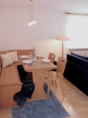 Un coin repas avec une table en bois mise pour deux personnes, un canapé et une lampe.