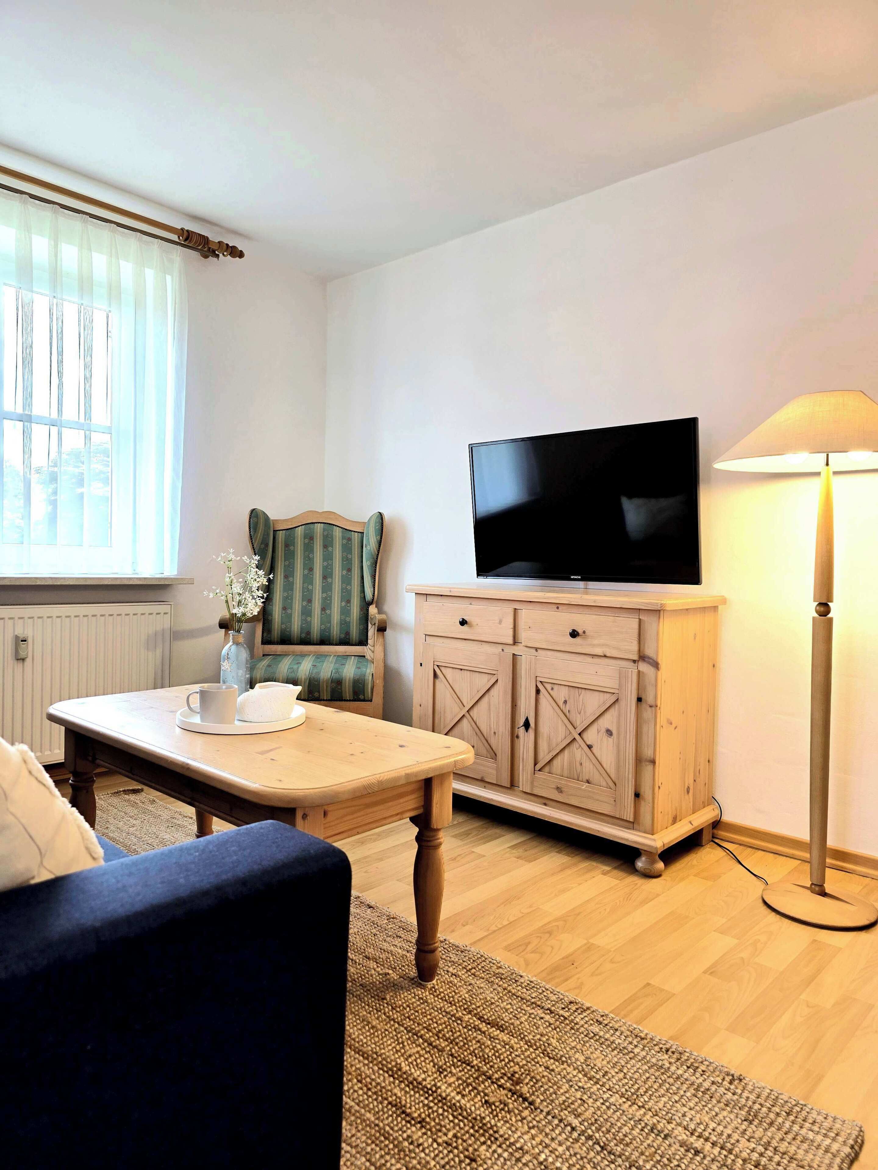 A living room with a television, a wooden cabinet, a lamp, a chair, and a coffee table.