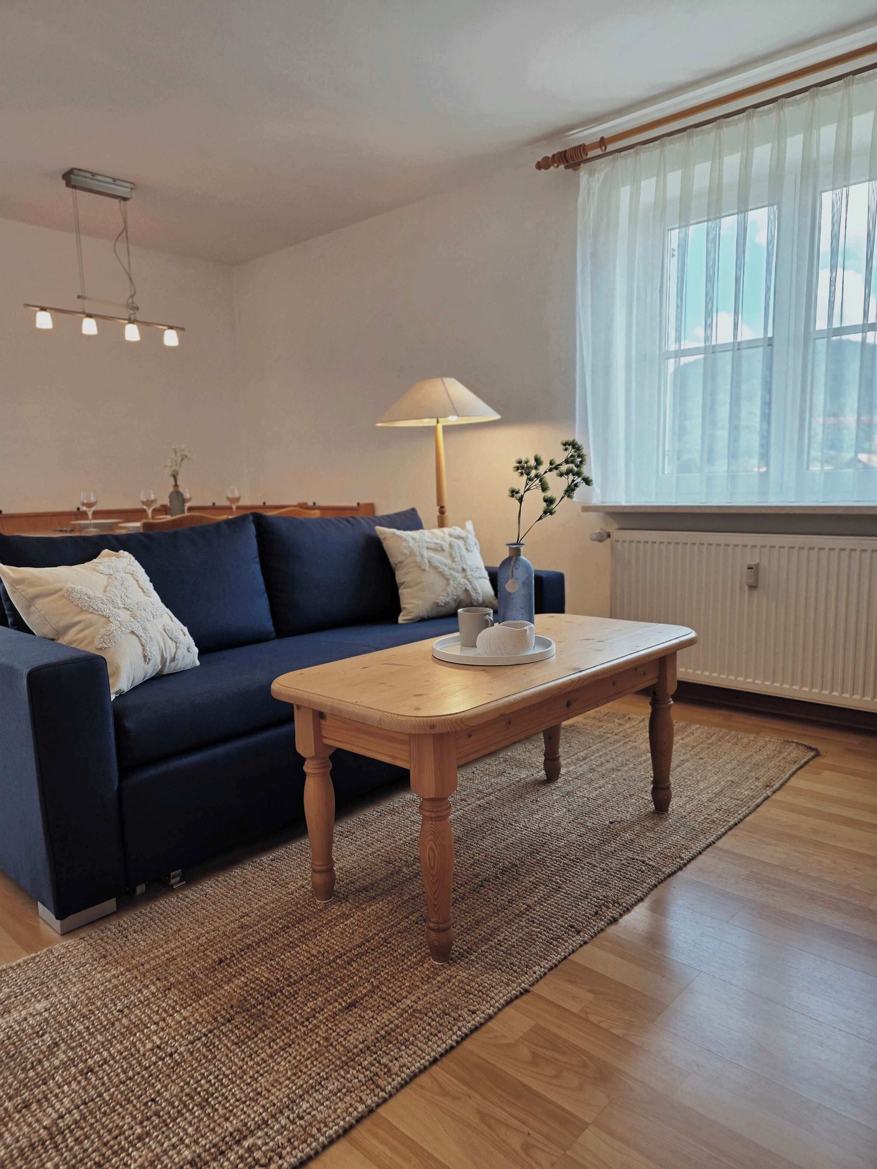 A living room with a sofa, a coffee table, a lamp, and a window with sheer curtains.
