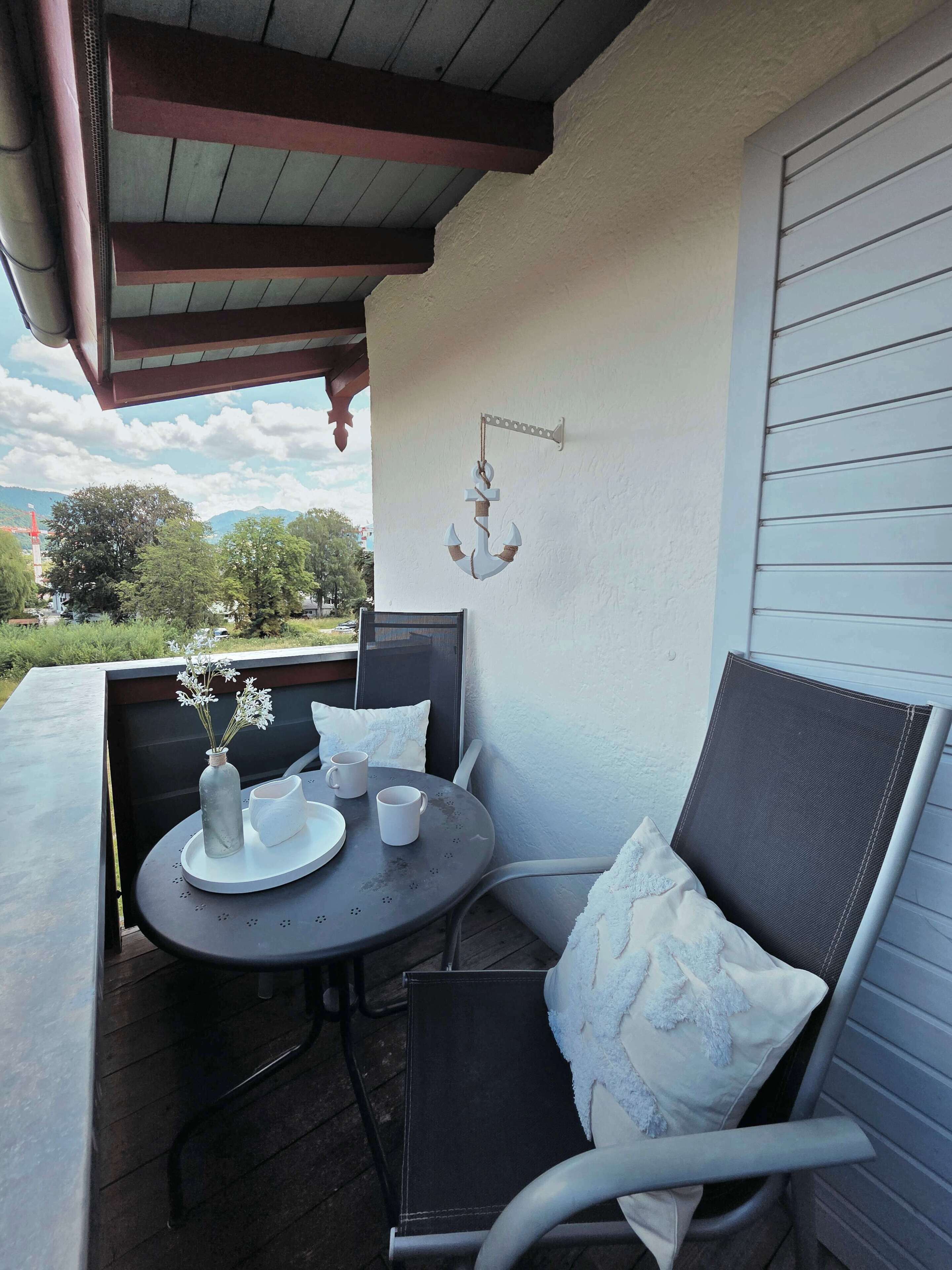 Een balkon met een tafel, stoelen en een decoratief hangend object.
