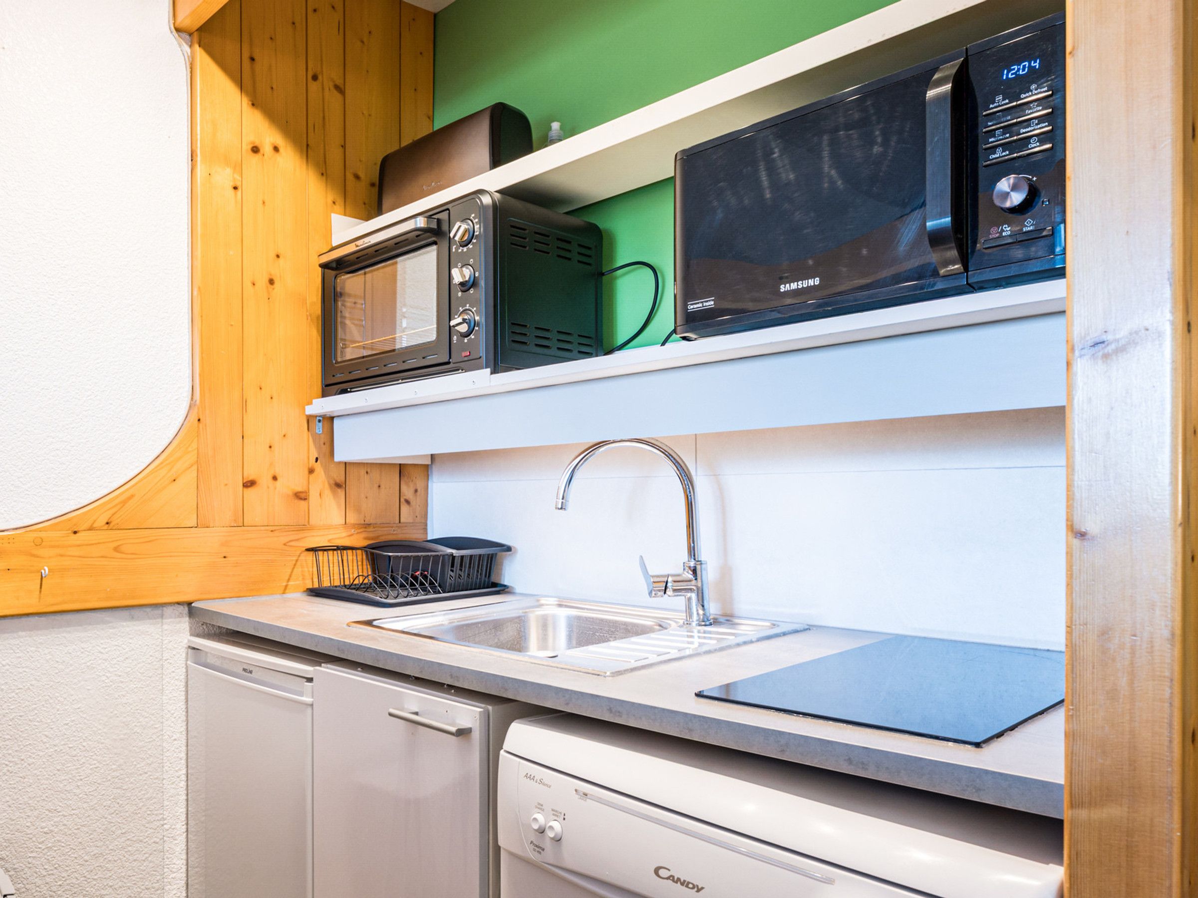 A compact kitchen with a dishwasher, a sink, and two microwaves on a shelf.
