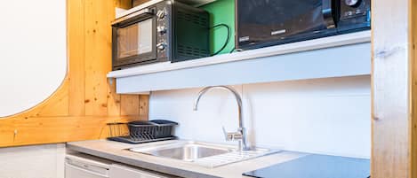 A compact kitchen with a dishwasher, a sink, and two microwaves on a shelf.
