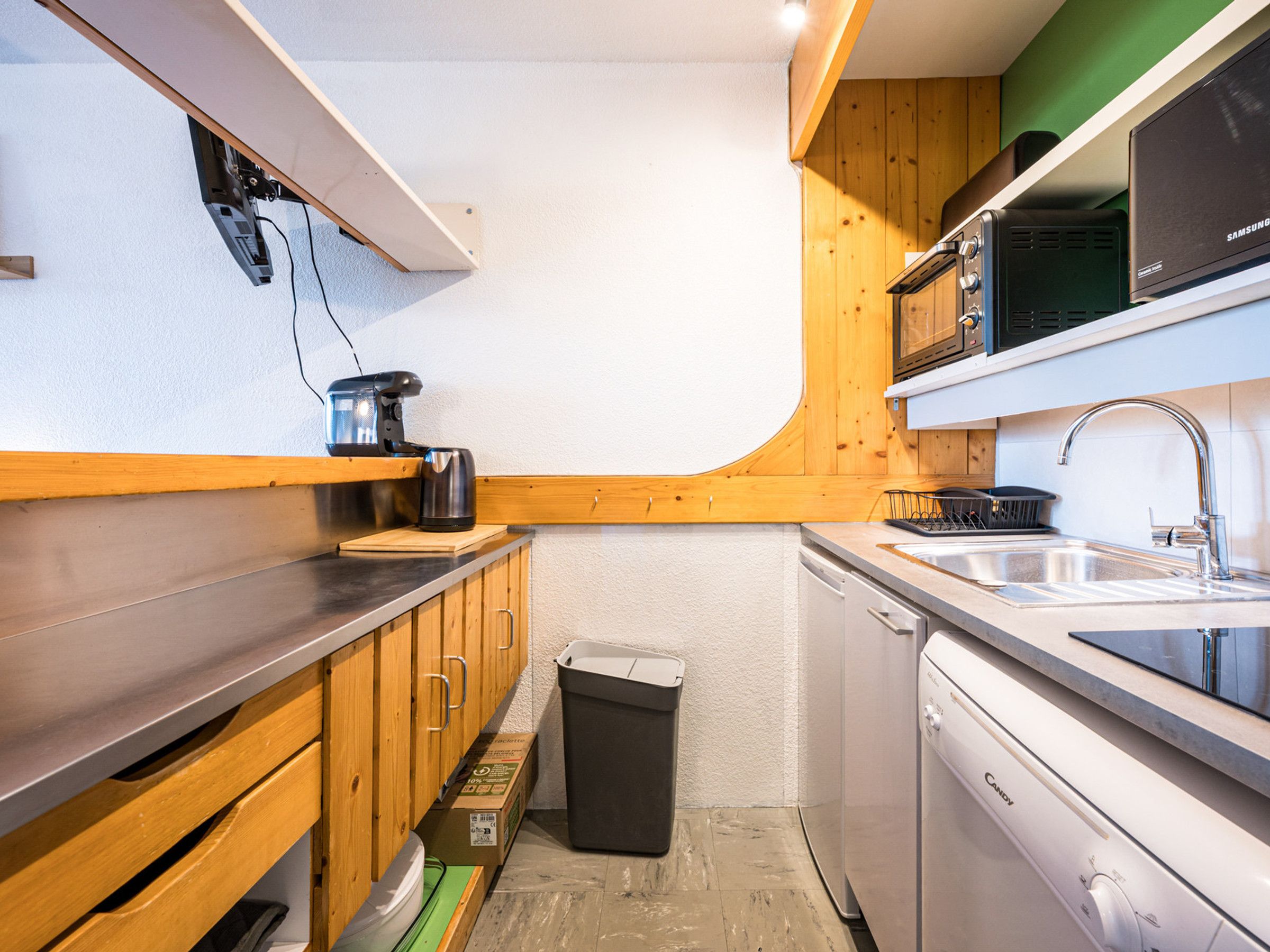 A compact kitchen with wooden cabinets, a dishwasher, a microwave, and a coffee maker.