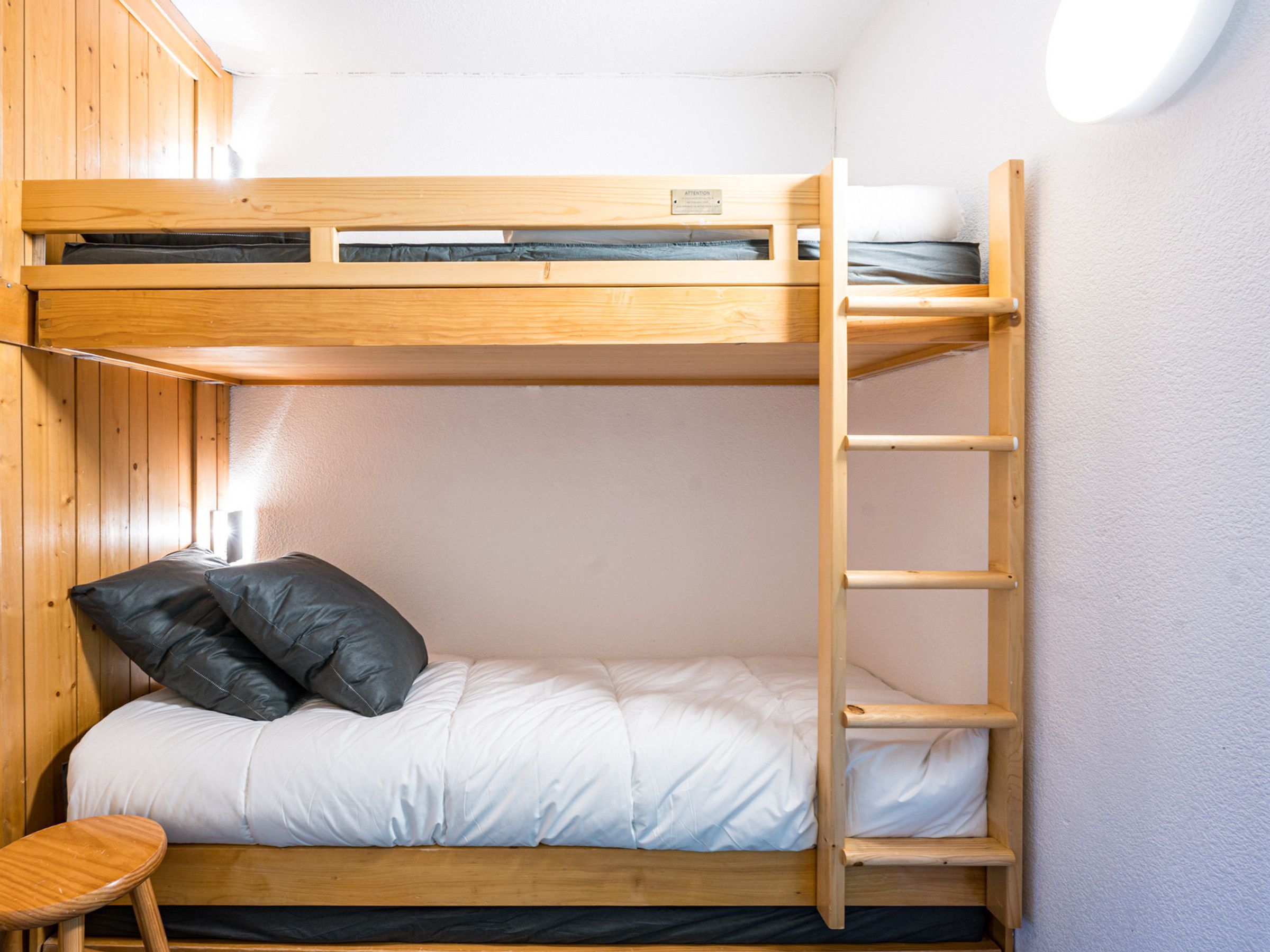 A bunk bed with a ladder, a small stool, and a pillow.