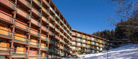 Un hotel de varios pisos con balcones, situado en una zona nevada con árboles al fondo.