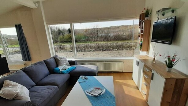 Uma sala de estar moderna com sofá, mesa de centro, TV e vista para um campo através de grandes janelas.