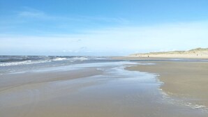 Uma praia com extensa faixa de areia, ondas suaves e céu claro.