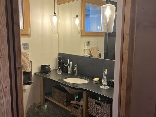 Ein Badezimmer mit einem Holzkosmetikschrank, einem Spiegel, einem Waschbecken und Pendelleuchten.