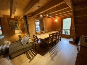 Ein gemütliches Blockhaus-Interieur mit einem Holzespeisetisch, Stühlen, einer Couch und einem Fenster mit Blick auf eine natürliche Landschaft.