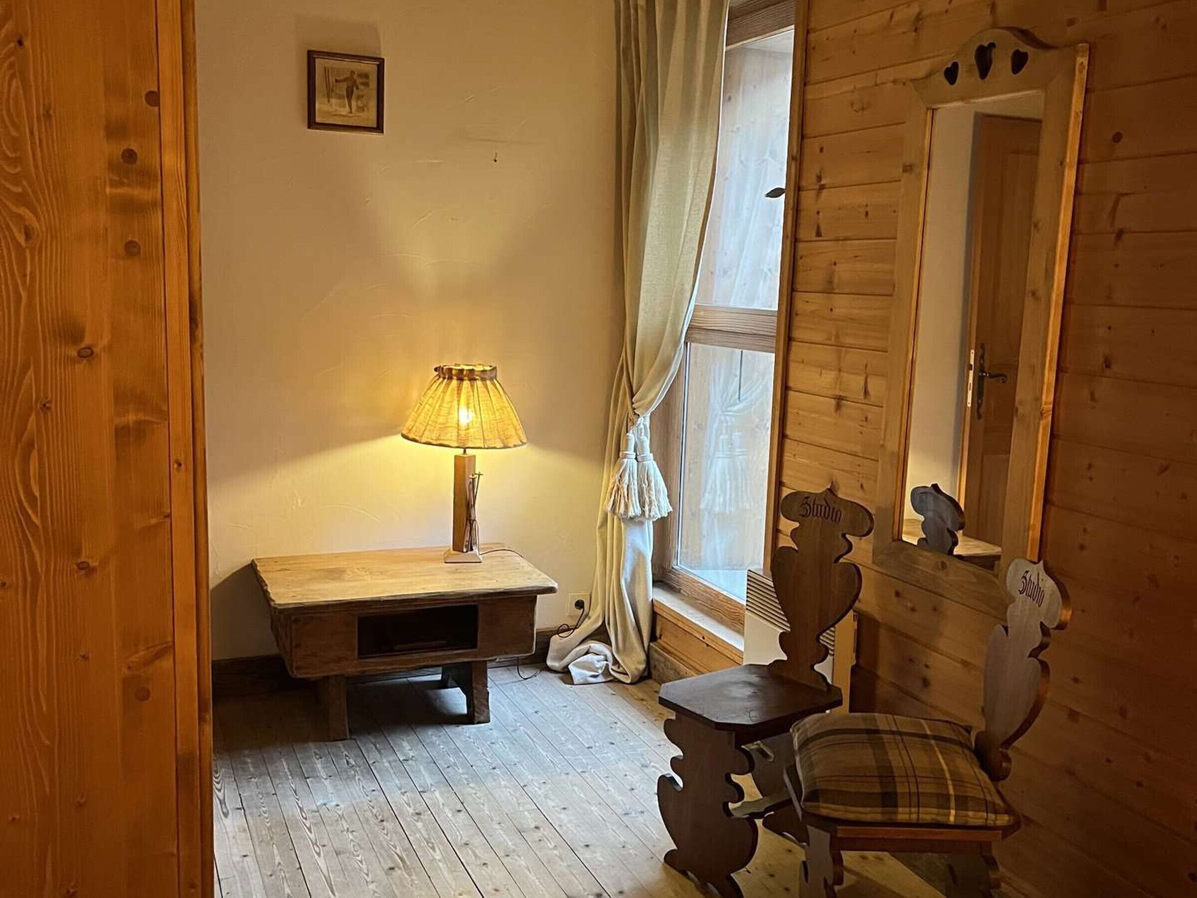 Une pièce en bois avec un bureau, une chaise, une lampe et un miroir au mur.
