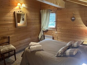 Ein gemütliches Holzblockhaus-Zimmer mit Bett, Stuhl, Spiegel und einem Fenster mit Vorhängen.