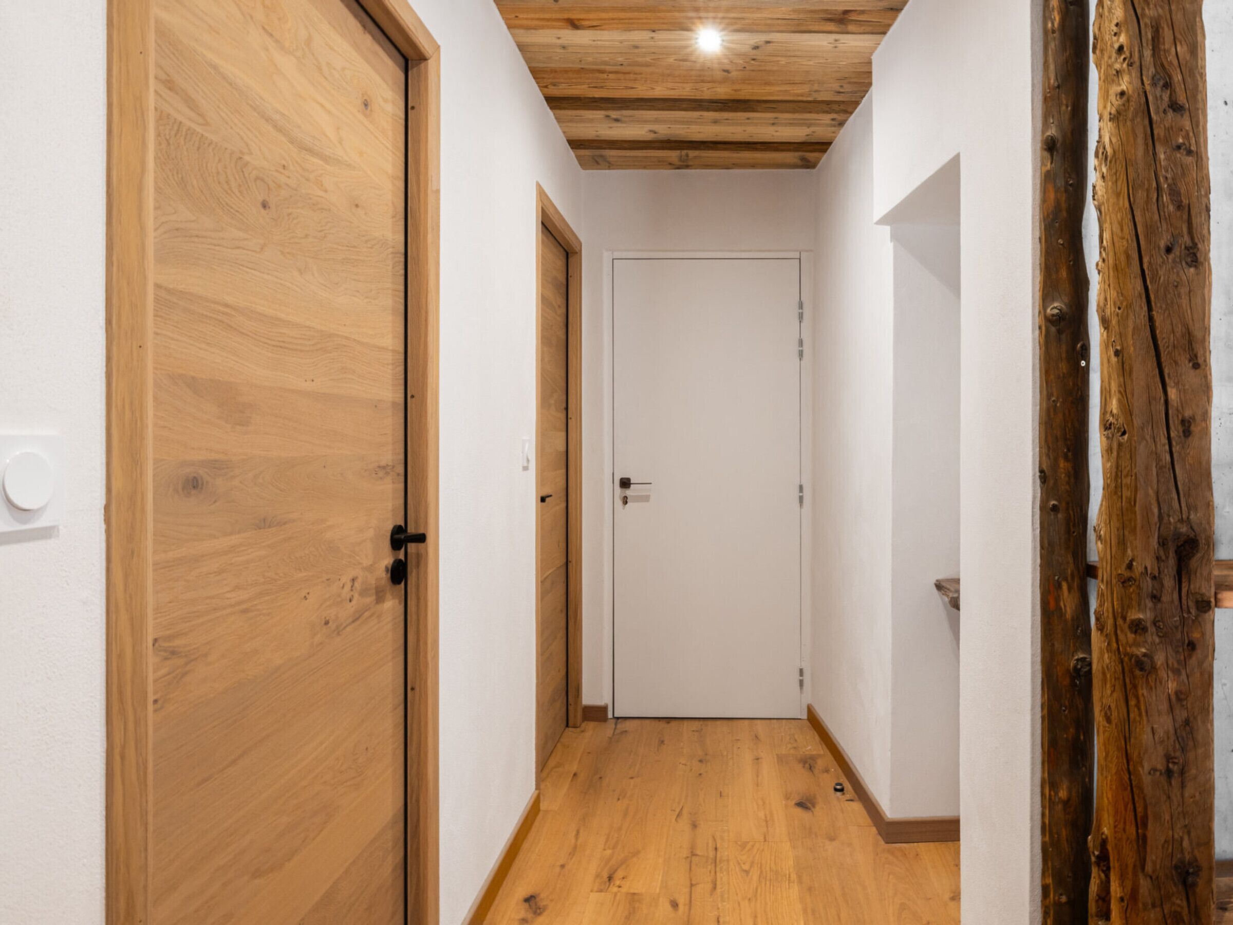 A narrow hallway with wooden flooring and doors, featuring a wooden ceiling and a visible electrical outlet.