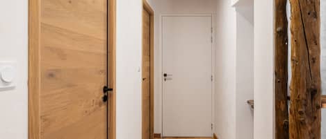 Un pasillo estrecho con suelo de madera y puertas, que cuenta con techo de madera y un enchufe visible.