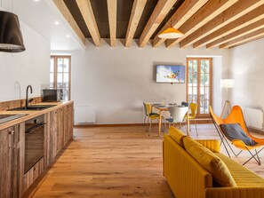 A modern kitchen with wooden beams, a dining area with yellow chairs, and a sofa. - Cozy apartment in the heart of the village - 5 guests (Le Monêtier-les-Bains)