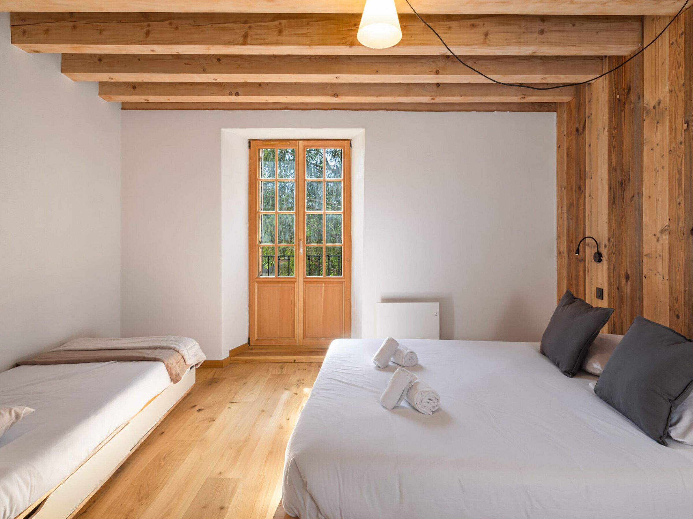 A bedroom with two beds, a wooden ceiling, a window, and a bedside lamp.