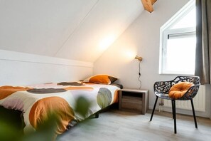 Une chambre à coucher avec un lit, une table de chevet, une chaise et une fenêtre avec des rideaux.