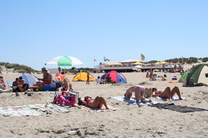A beach with tents, umbrellas, and people sunbathing. - Holiday apartment with 3 bedrooms (Ouddorp)