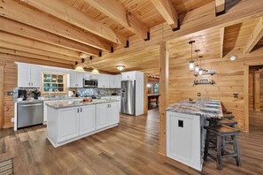 A spacious kitchen with wooden beams, white cabinets, and a central island with stools. - Pet-Friendly, private cabin with a hot tub, firepit and game room! (Ellijay)