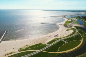 An aerial view of a coastal area with a beach, roads, and a large body of water. - Cabin in Berkhout with swimming pool (Berkhout)
